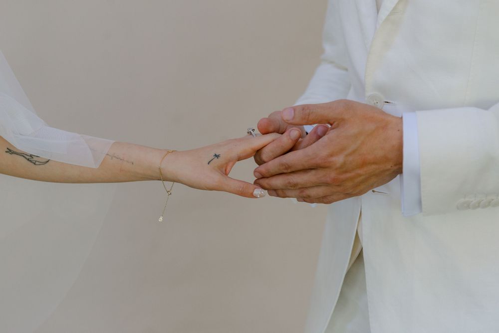 Close-up shot of hands exchanging wedding rings between two people in white formal attire.
