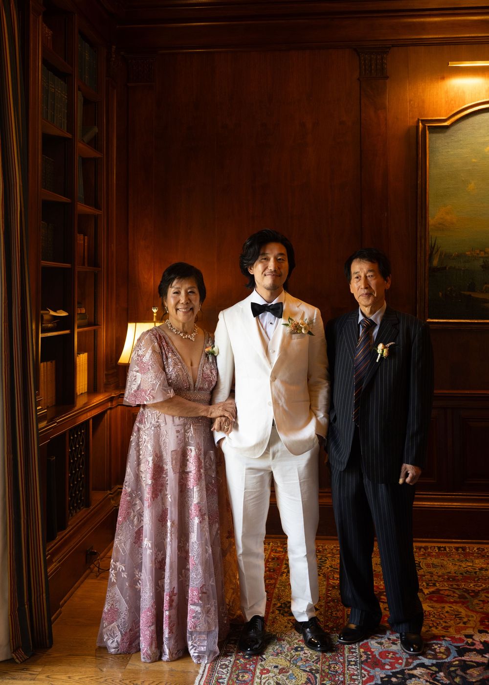 Wedding party poses in formal attire inside a wood-paneled room.