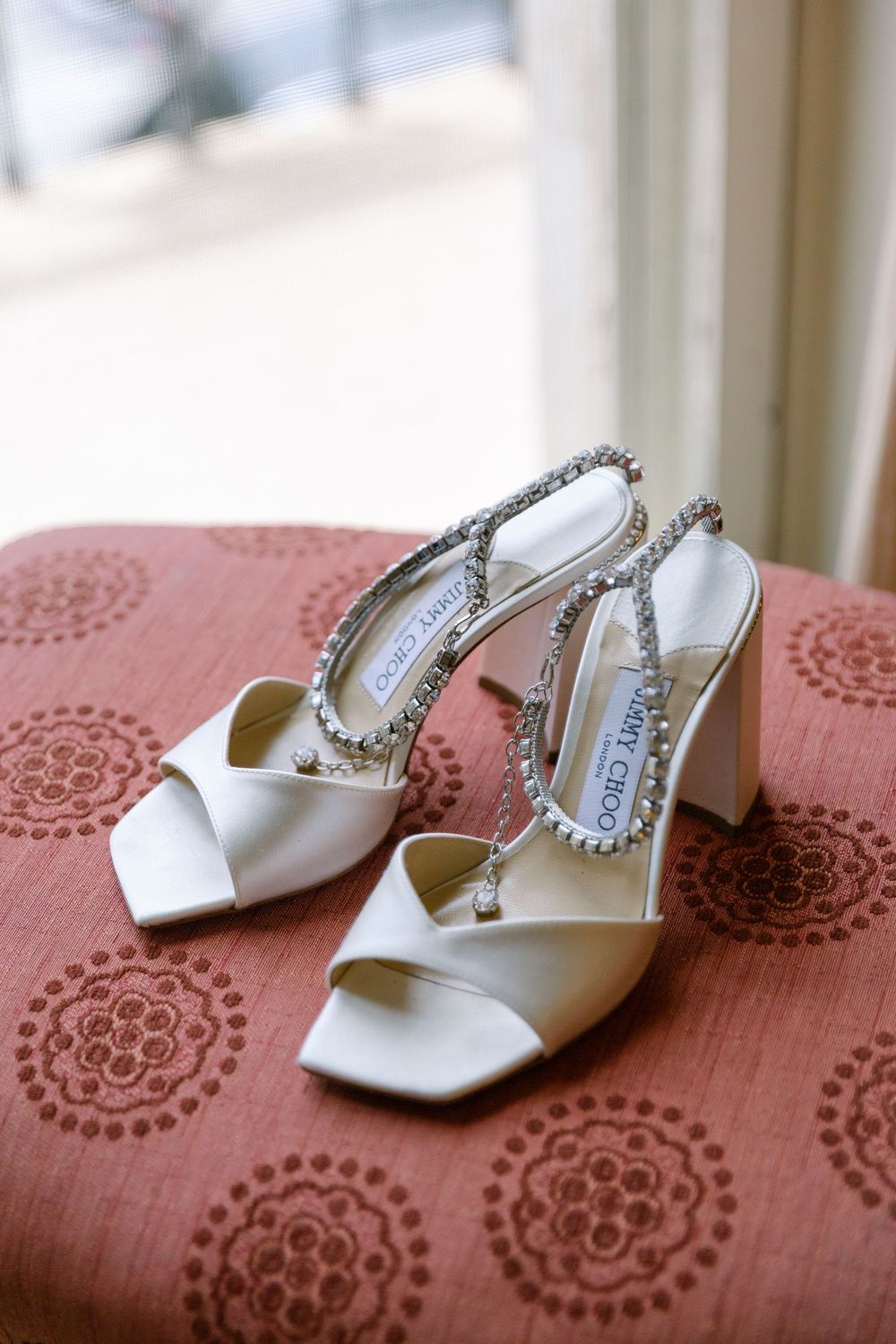 White satin wedding shoes with crystal details on coral patterned fabric.