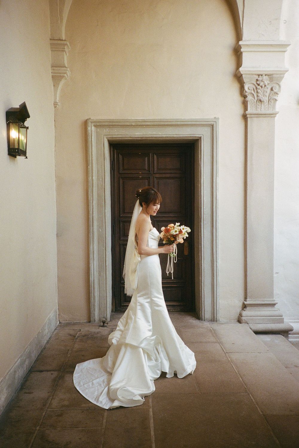 Elegant bride holding a bouquet while walking through an ornate archway.