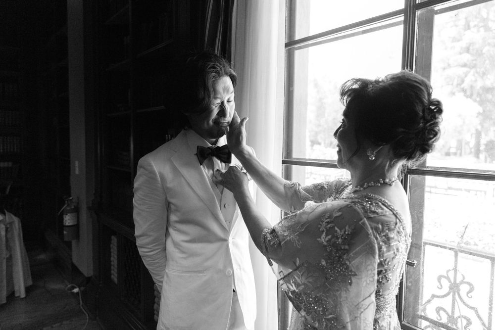 An intimate black and white wedding preparation moment near a sunlit window.