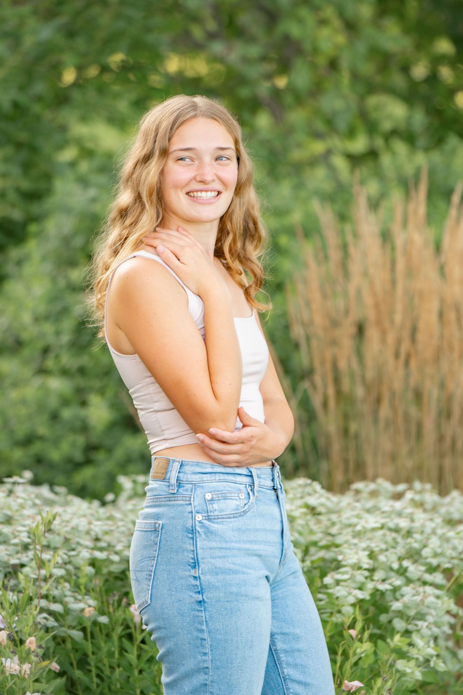 Candid outdoor portraits in casual denim and white top surrounded by blooming wildflowers and tall grass.