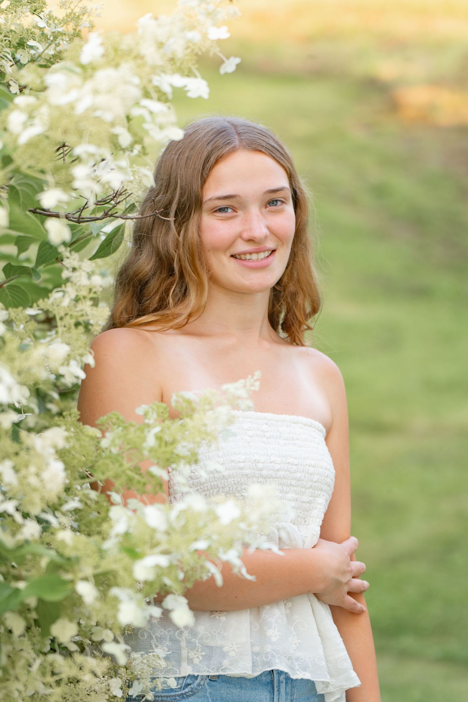 Outdoor portrait against a flowering white bush wearing a white summer top and denim in warm natural lighting.