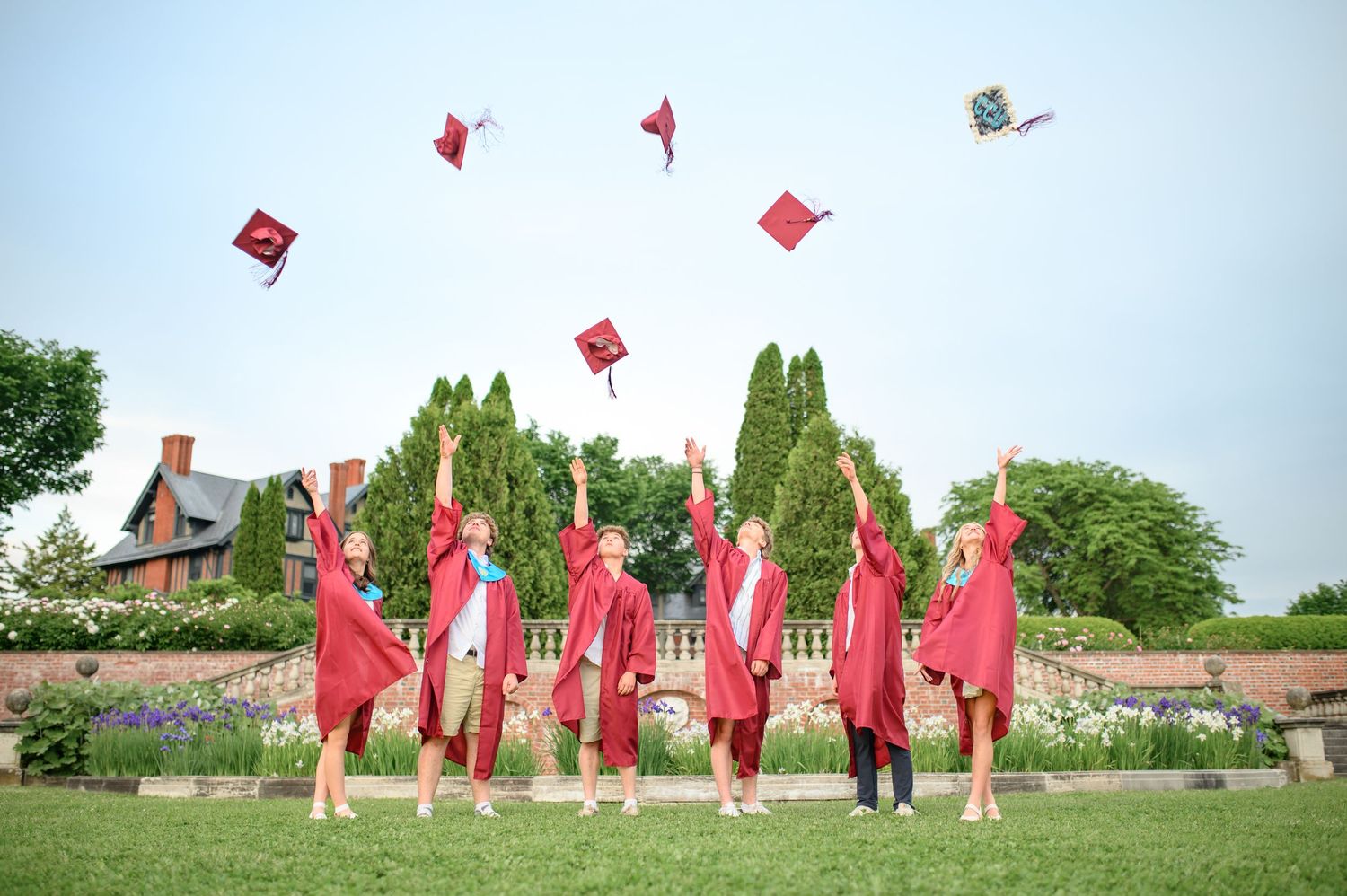 Graduates in red robes throw their mortarboards into the air during graduation celebration.