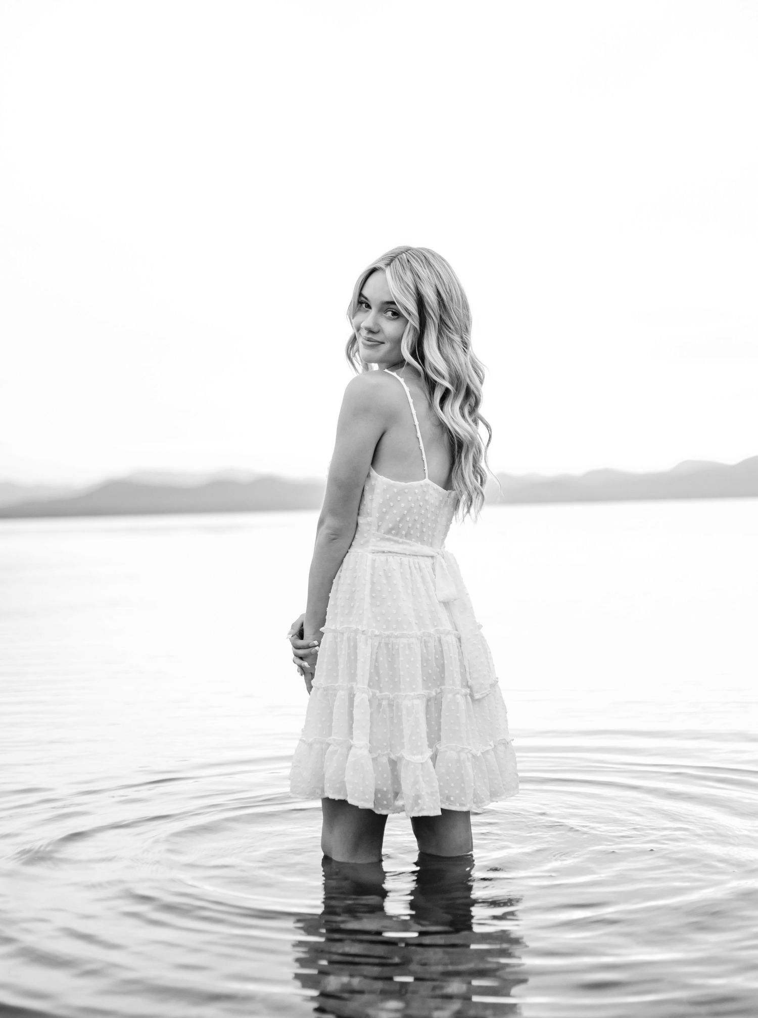 A artistic black and white photo series of a person in a white dress standing in tranquil water.