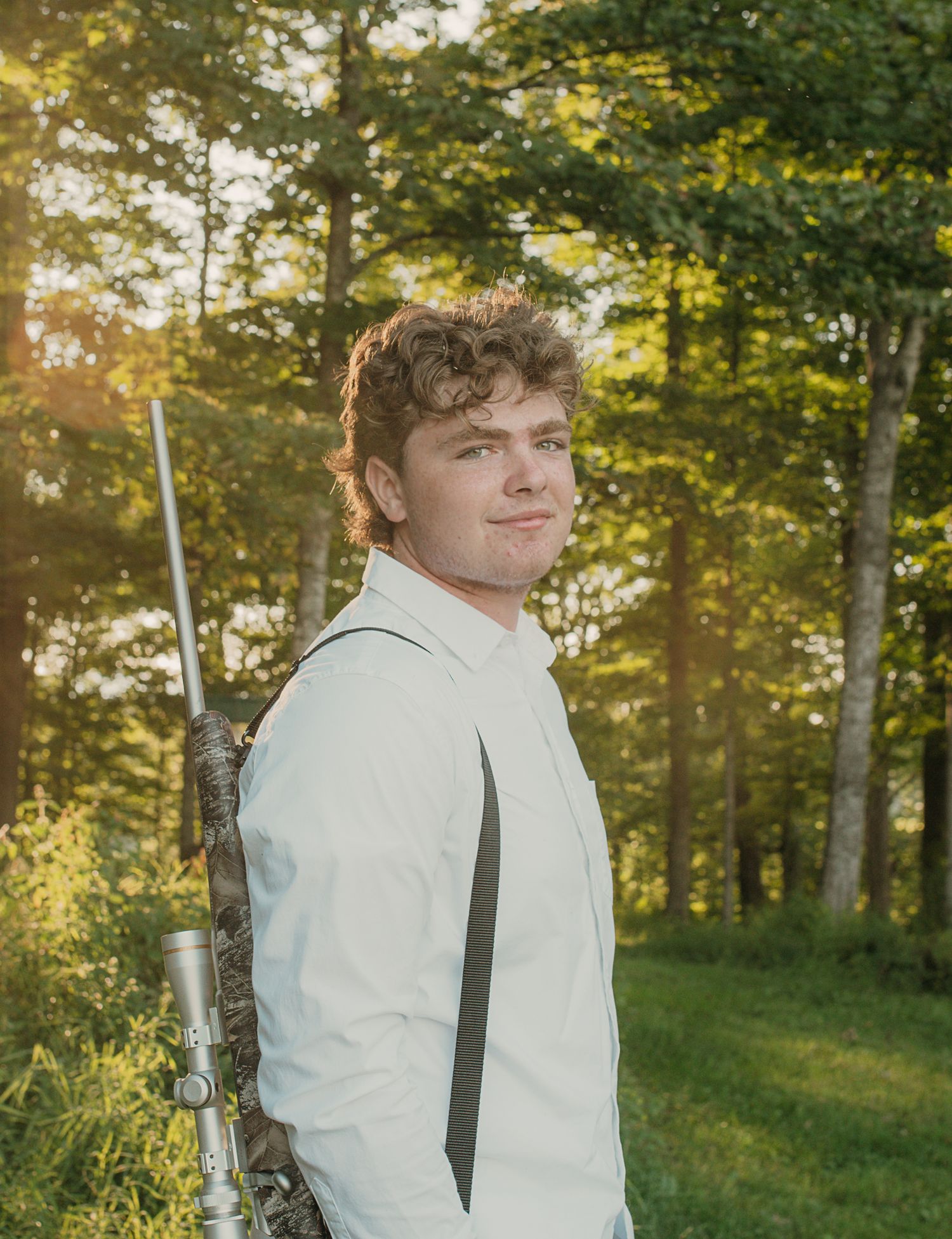 A portrait taken in a sunlit forest setting featuring a white button-down shirt against a natural backdrop.