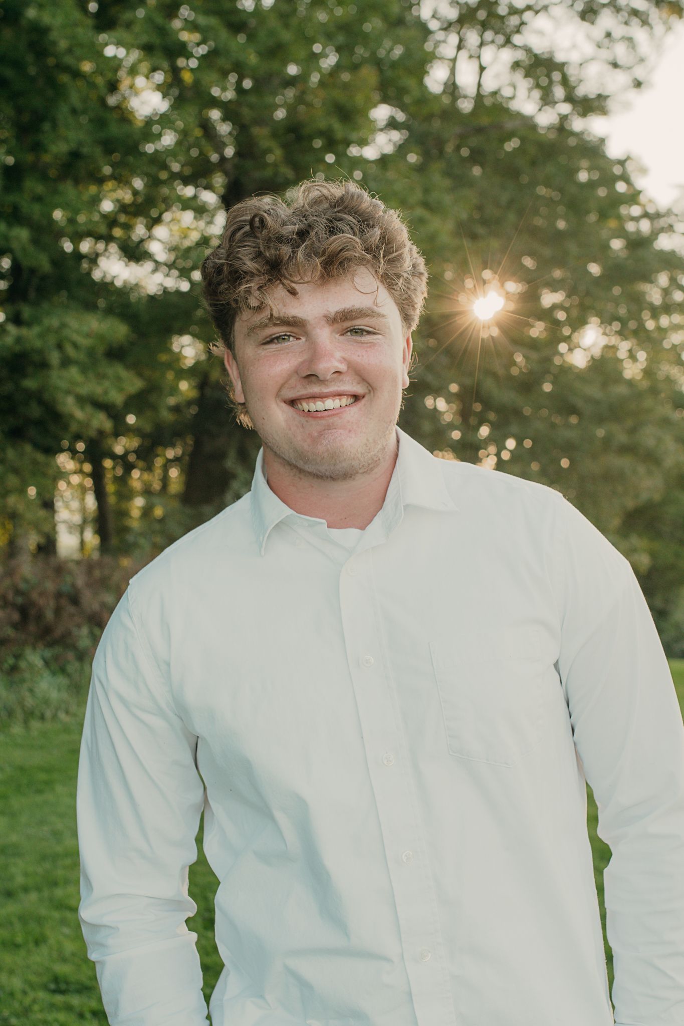 Close-up outdoor portrait taken in natural lighting with a white button-down shirt and forest greenery in background.