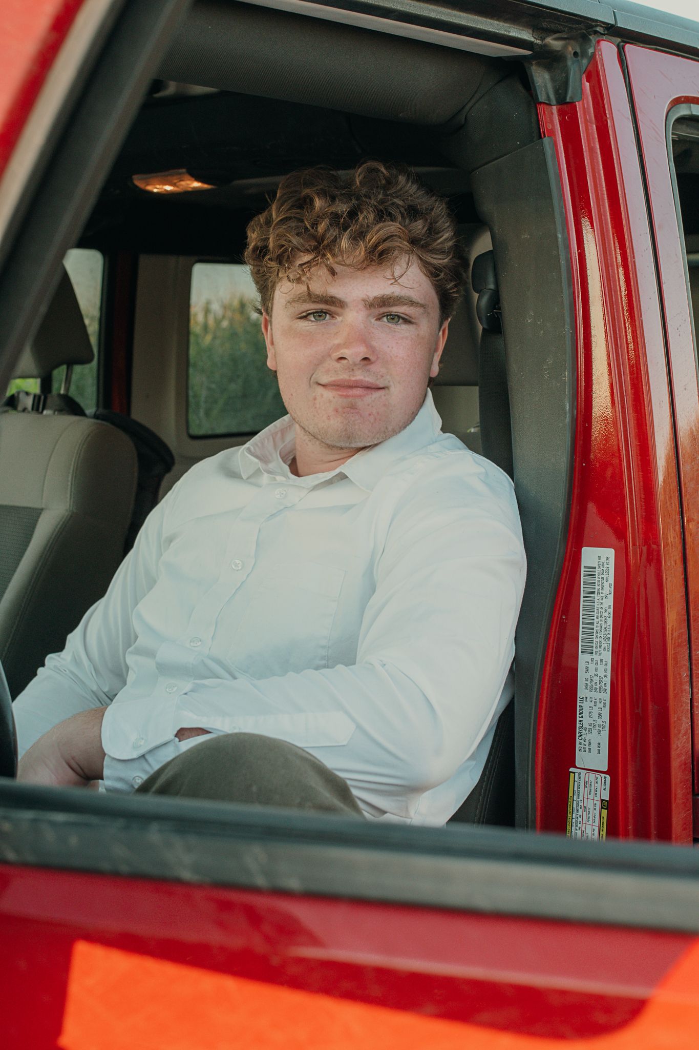 Someone in a white dress shirt sits in the driver's seat of a bright red vehicle.