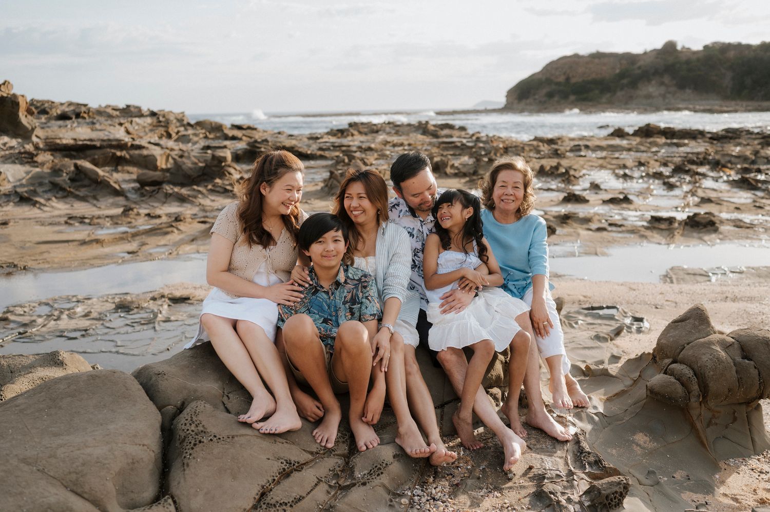 A group sits together on rocky coastal beach with ocean and cliffs in background during golden hour.