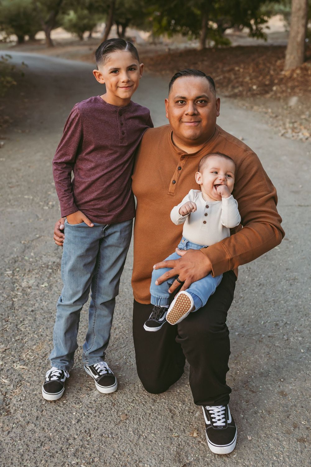 A touching family moment captured outdoors on a path surrounded by fall foliage.