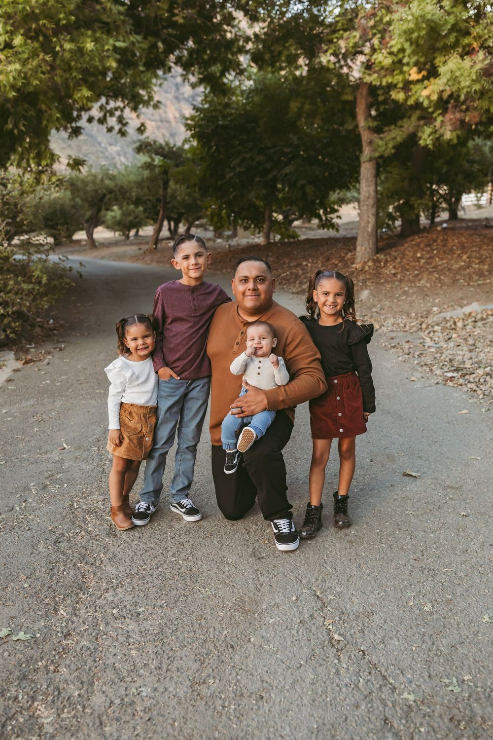 A family group poses together on a tree-lined path during an autumn outdoor photoshoot.