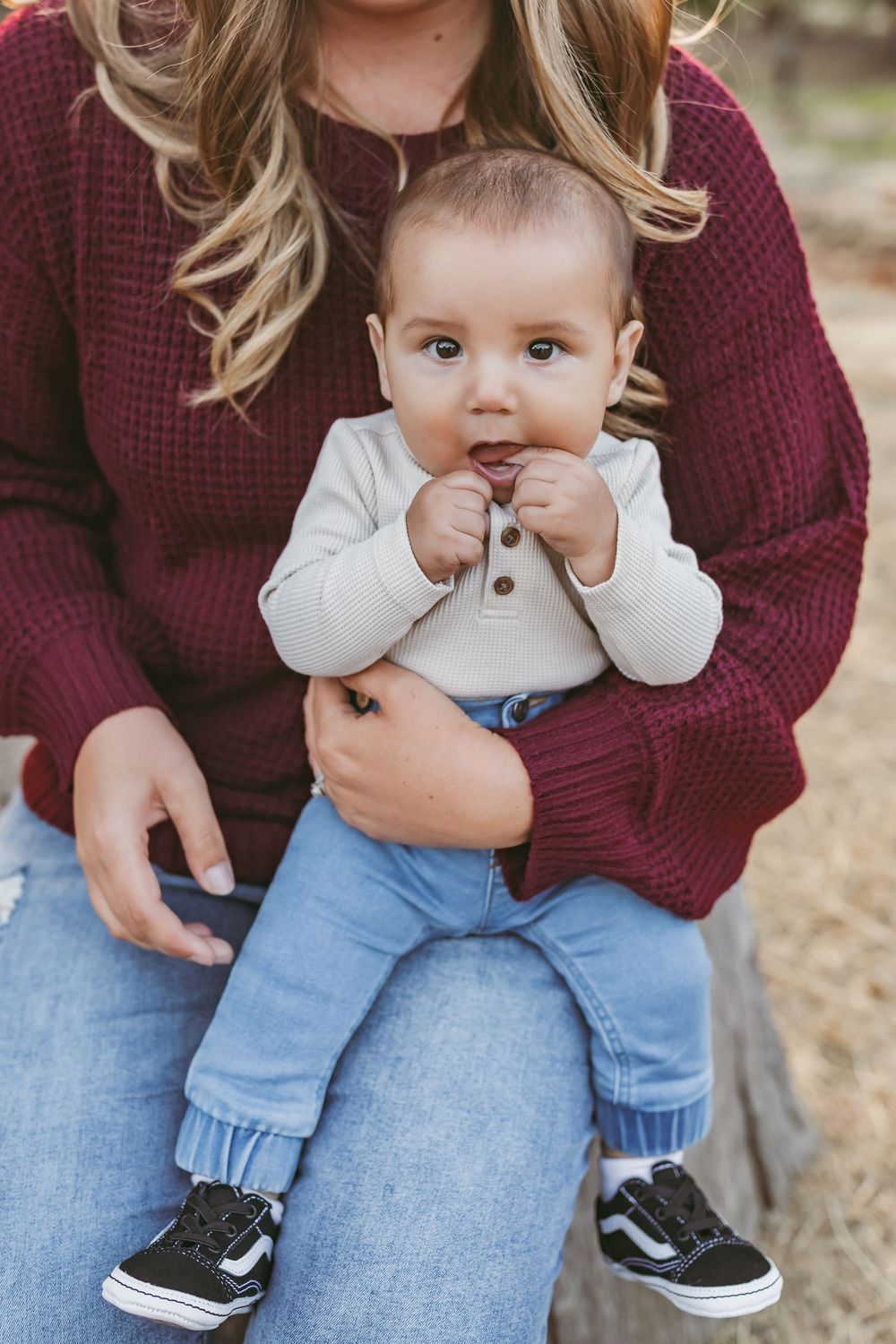 Baby in a white top and sneakers sits on parent's lap wearing burgundy sweater and blue jeans.