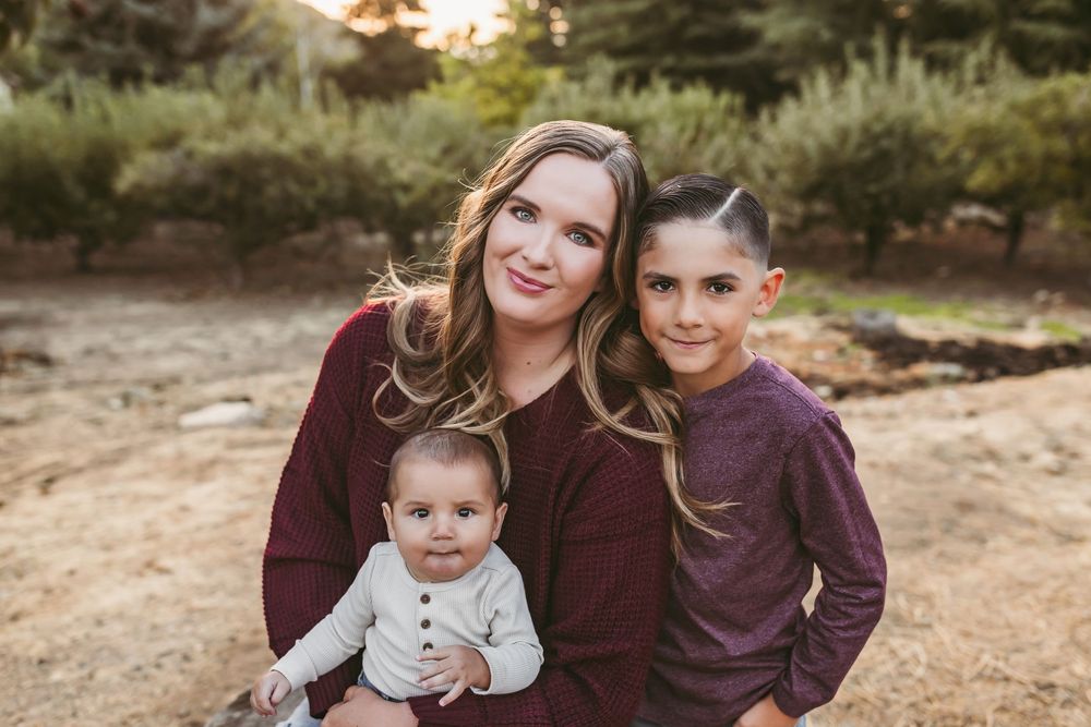 Family wearing coordinating burgundy and white outfits pose together outdoors during sunset photoshoot.