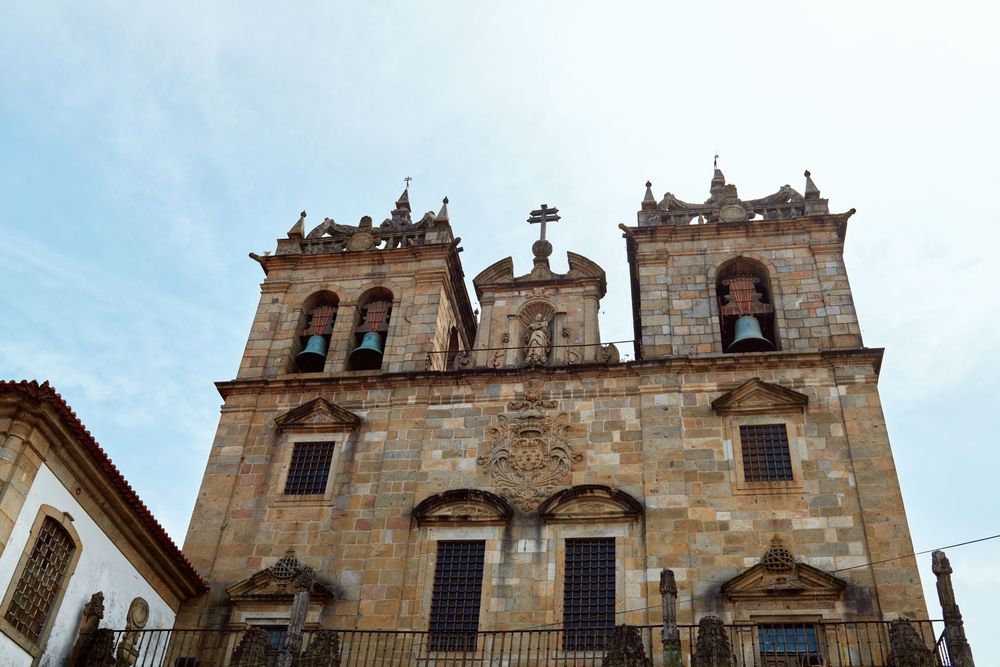 Historic ornate stone Catholic church facade with twin bell towers against cloudy sky.
