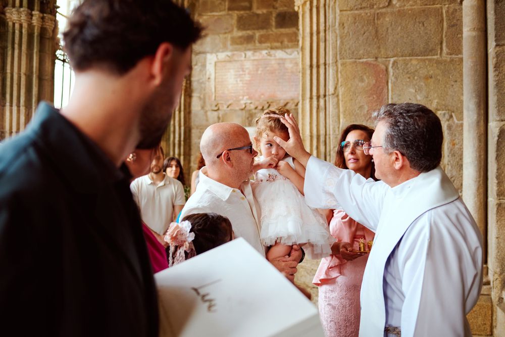 Priest blessing infant during baptism ceremony inside historic stone church with family gathered.