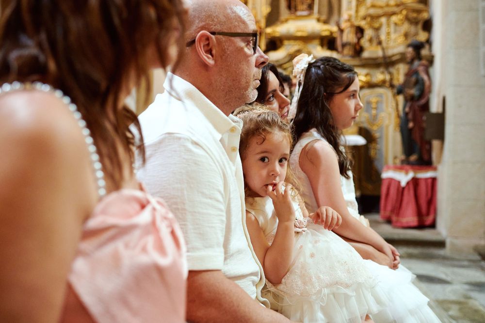 Father sitting with two young girls in white dresses during church baptism ceremony.