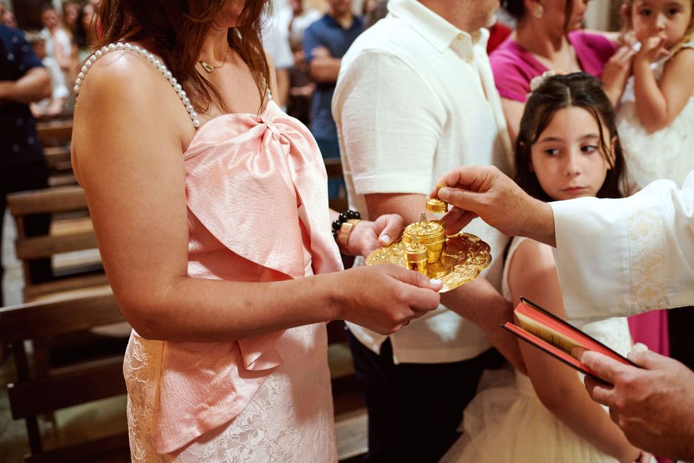 Child receiving golden baptism gifts during religious ceremony inside decorated church.