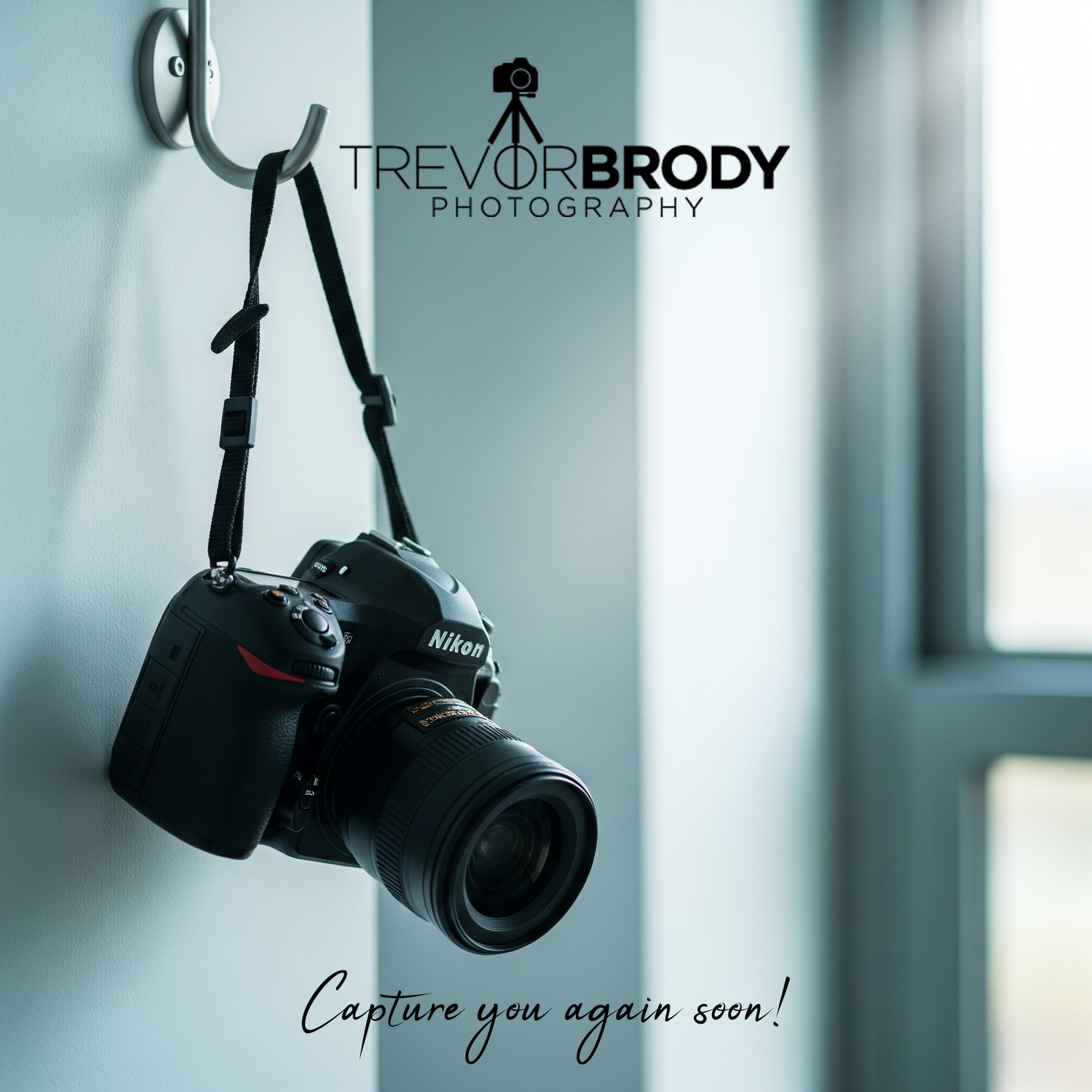 A Nikon DSLR camera with lens hangs by its strap against a blue-tinted wall with Trevor Brody Photography branding.