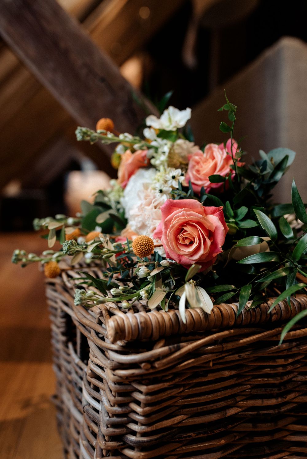 Pink roses and mixed flowers arranged in rustic wicker basket.