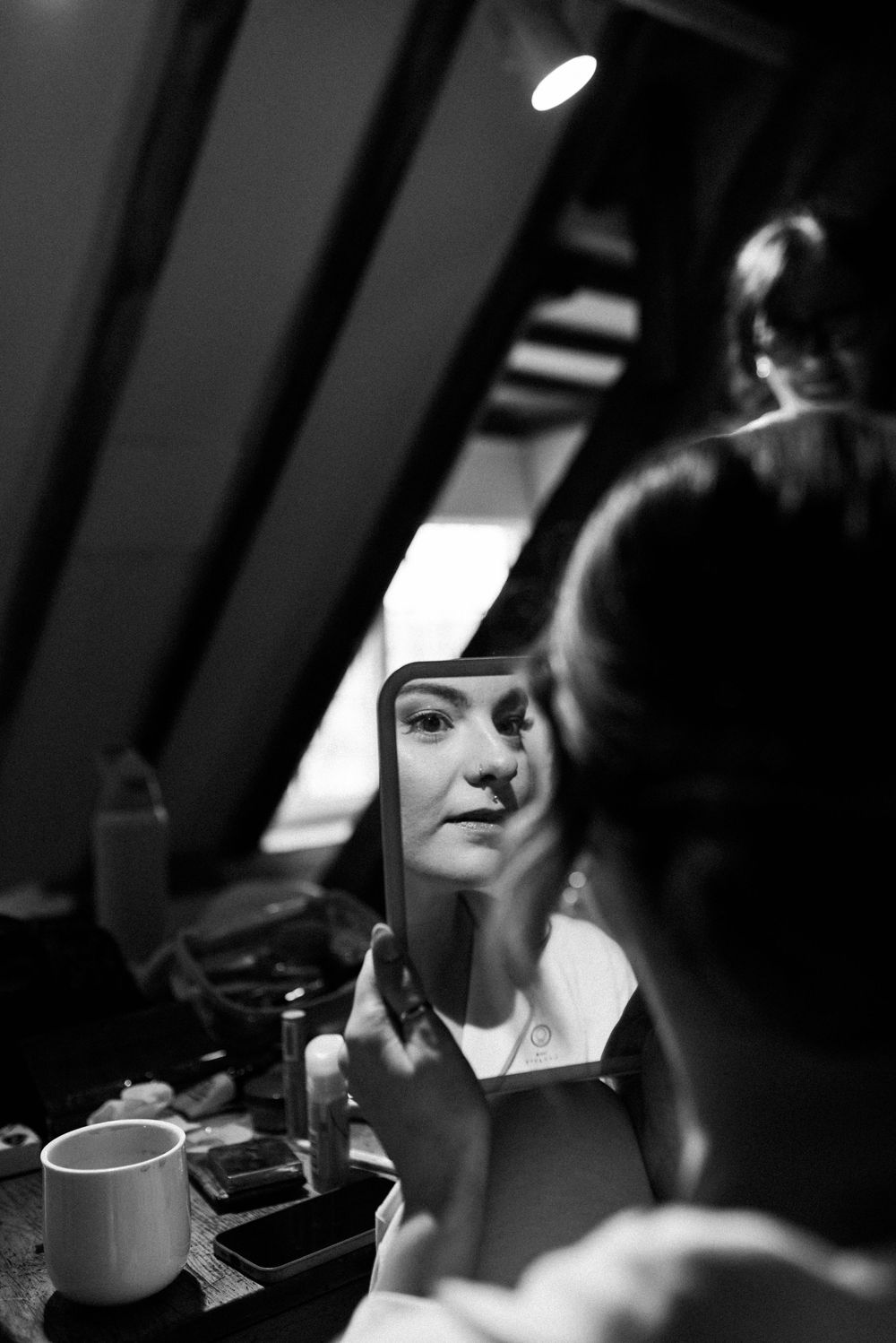 Atmospheric black and white photo of someone looking in a makeup mirror during preparations.