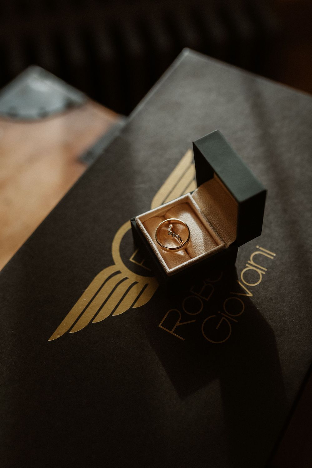 Wedding rings displayed in an elegant box with a gold wing logo on a dark surface.