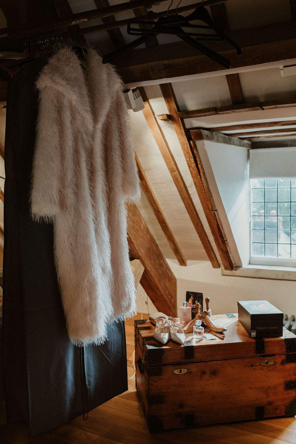 White furry coat hanging in rustic room with wooden beams and chest.