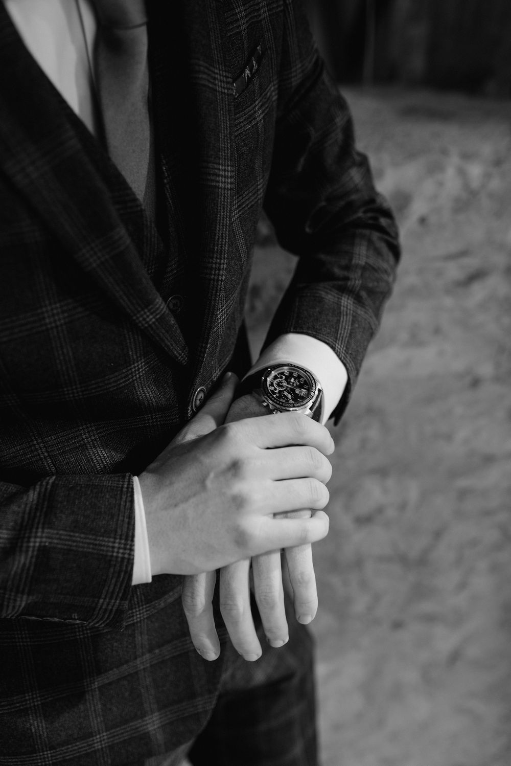 Close-up shot of hands adjusting a wristwatch while wearing a plaid suit jacket.