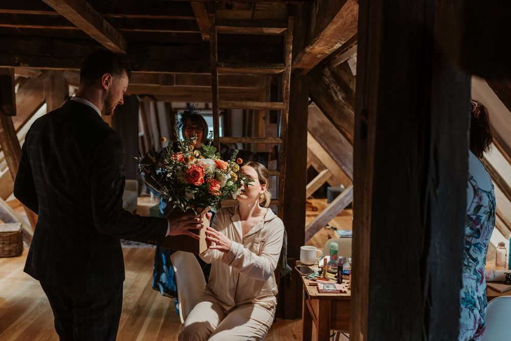 A candid moment captured in a rustic attic space with wooden beams and soft lighting showing flowers.