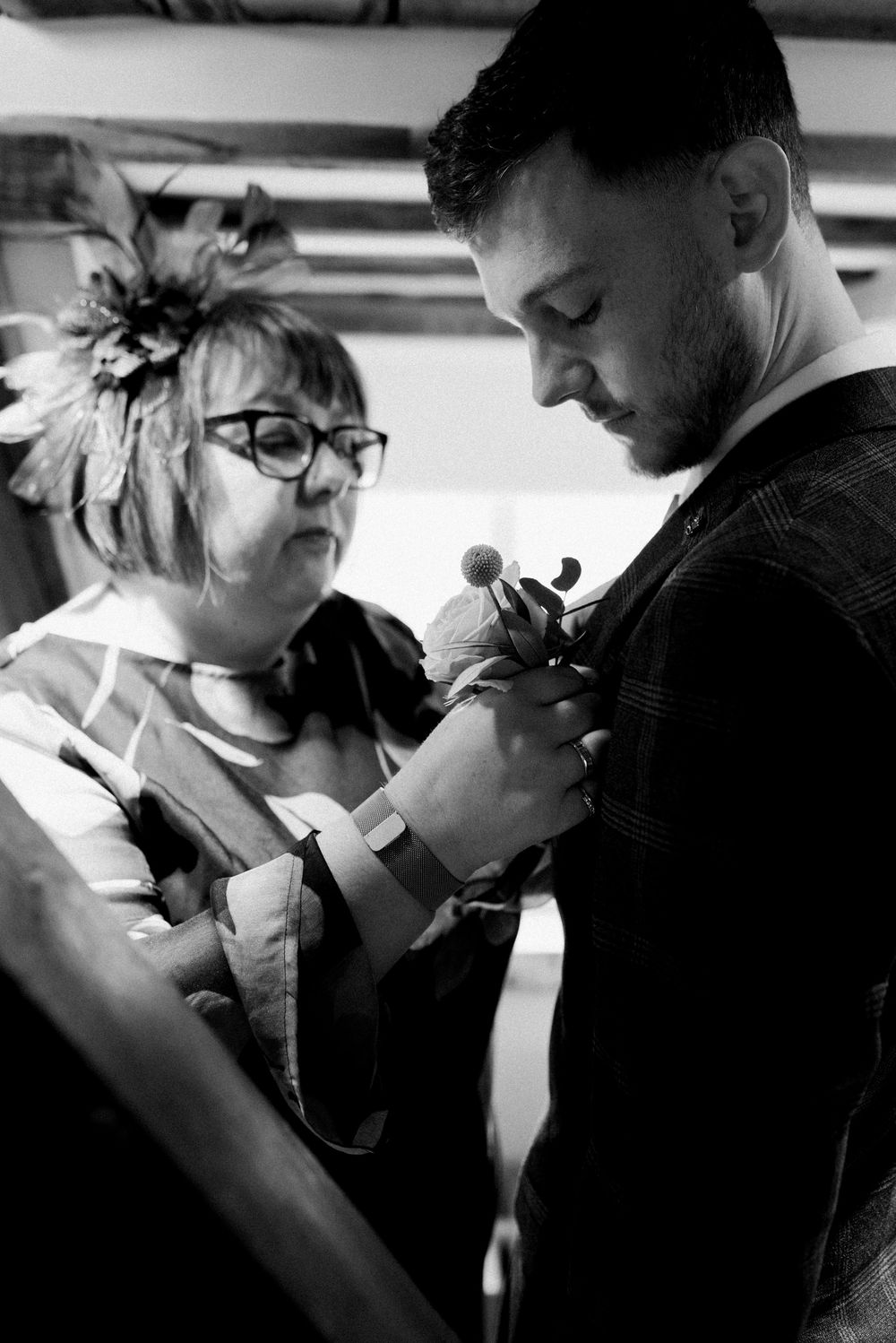 A black and white candid moment of wedding preparations with boutonniere being pinned.