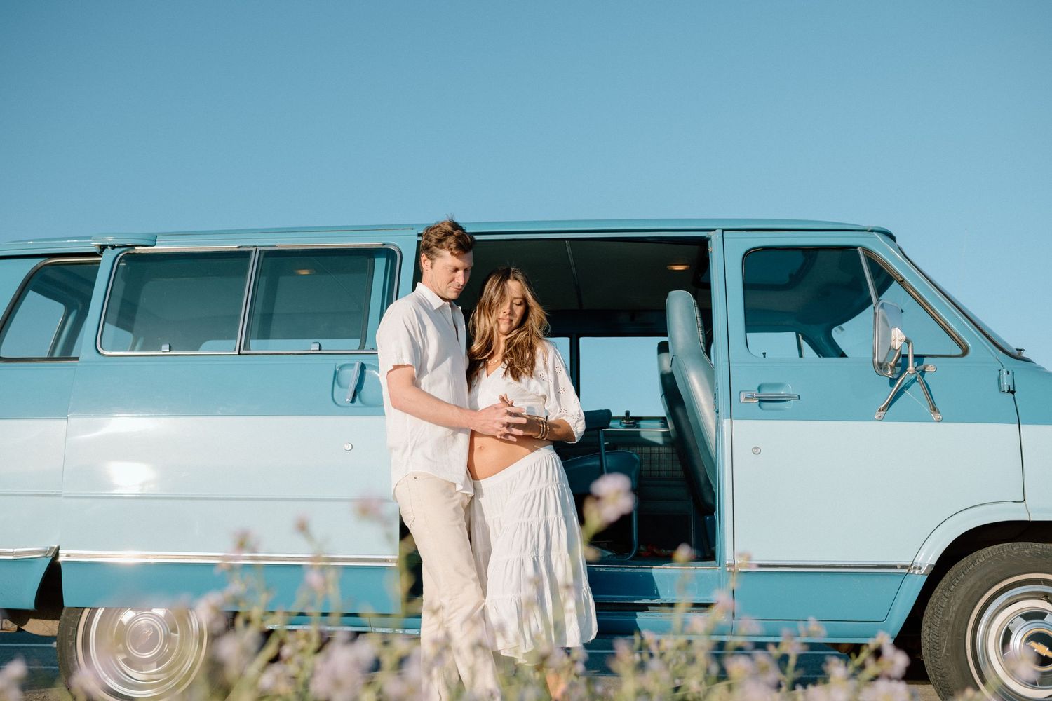 Light blue vintage station wagon parked at beach with surfboards and young passengers enjoying summer vibes.