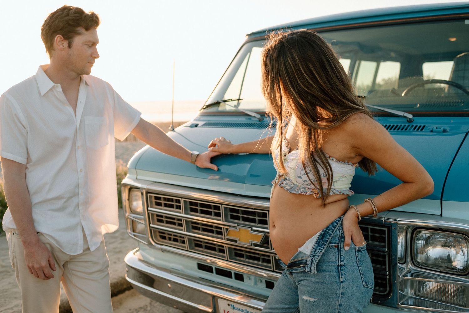 A couple poses playfully by a vintage blue truck during a golden hour photoshoot.