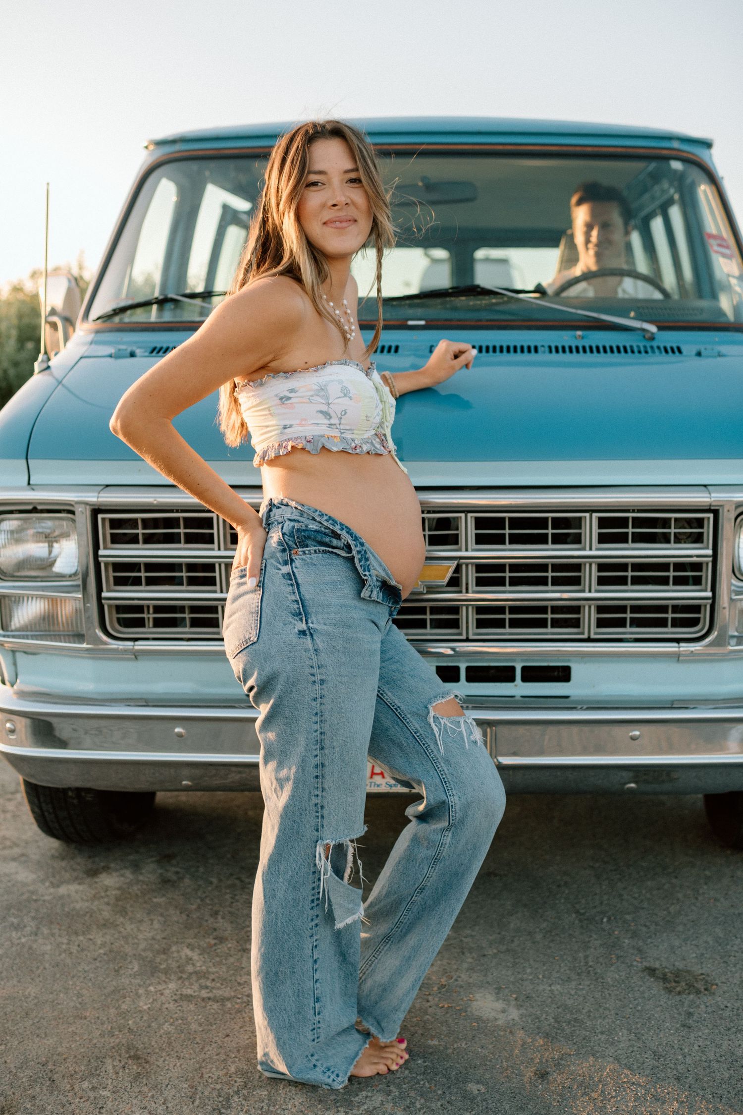 A retro-style photoshoot featuring someone in denim jeans posing with a classic blue pickup truck.