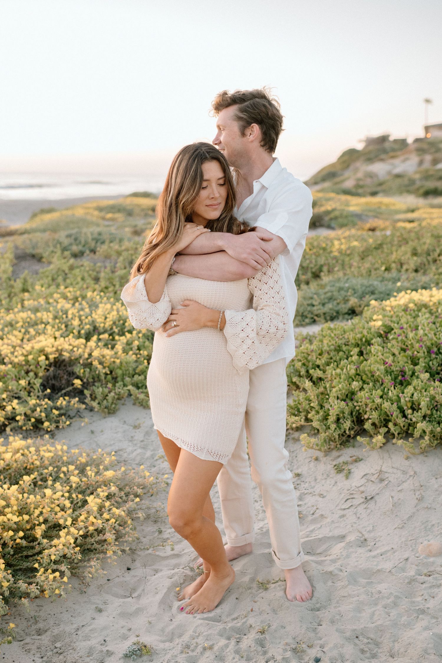 A romantic maternity photo session in blooming coastal wildflowers at sunset.