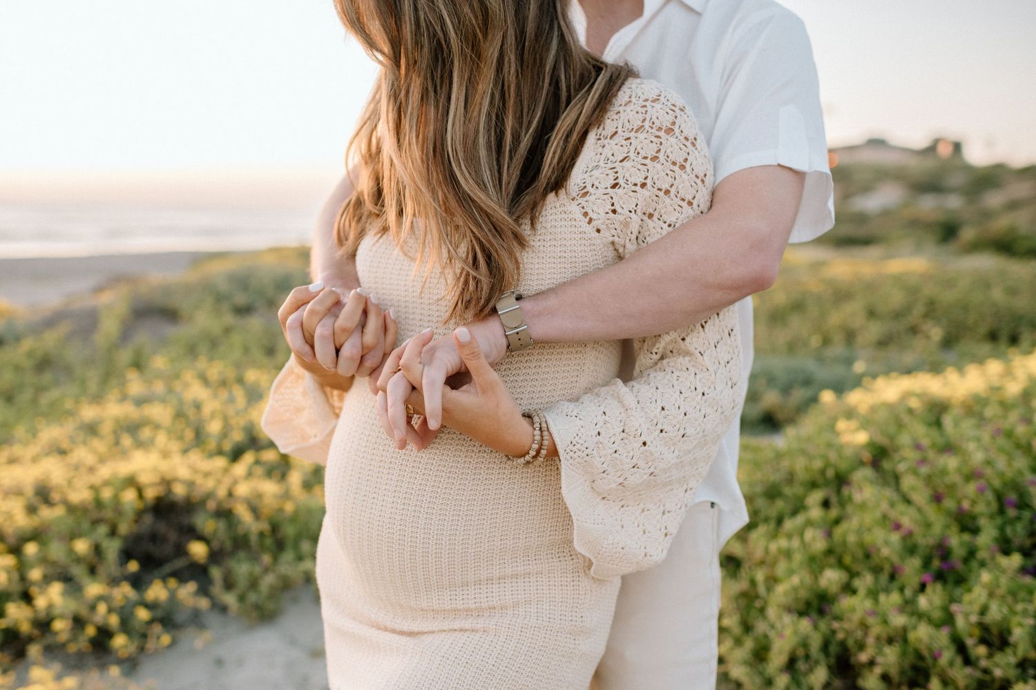 A tender maternity moment captured among coastal flowers during golden hour.