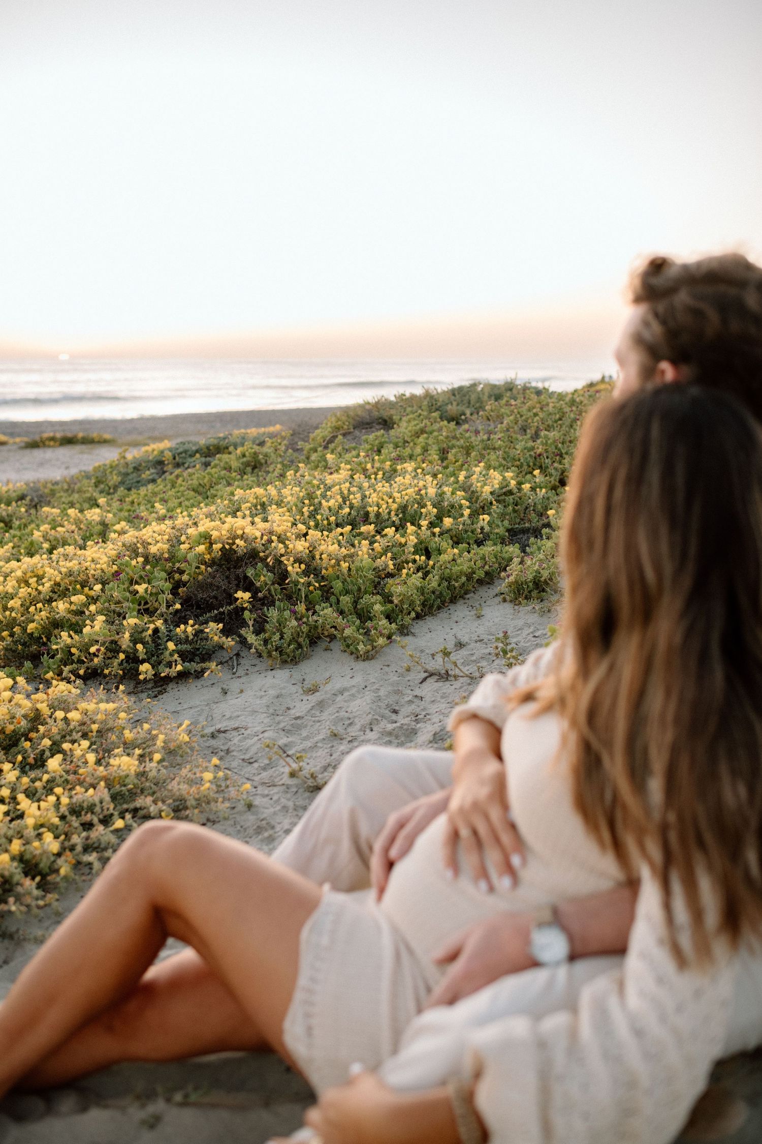A relaxed beachside moment at sunset with yellow wildflowers growing along the sandy shore.
