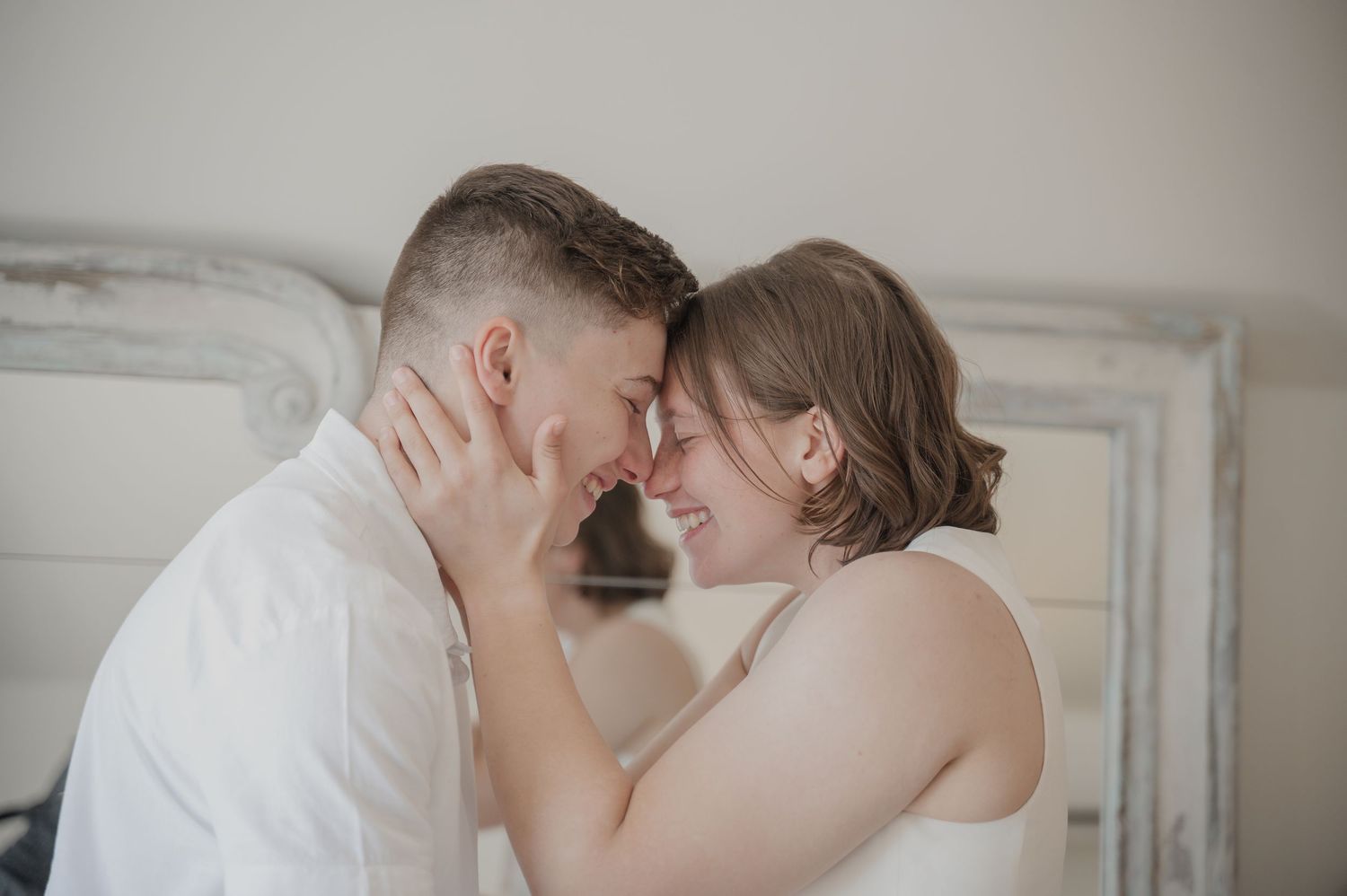 A tender intimate moment between a couple in white, touching foreheads while sharing an emotional embrace.