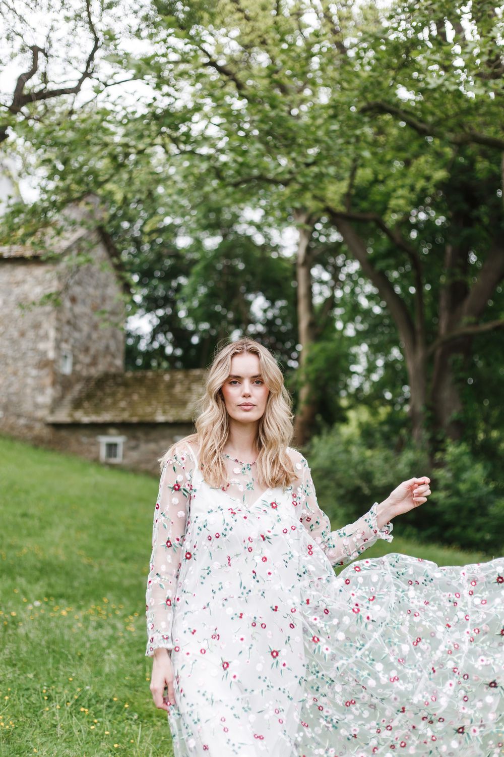 A woman in a white floral dress poses gracefully in a lush green garden setting during a photo session.