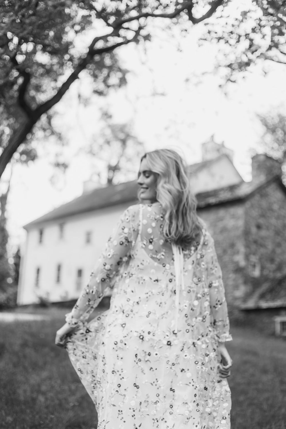 A child wearing a floral print dress twirls playfully outdoors with a white house visible in the background.