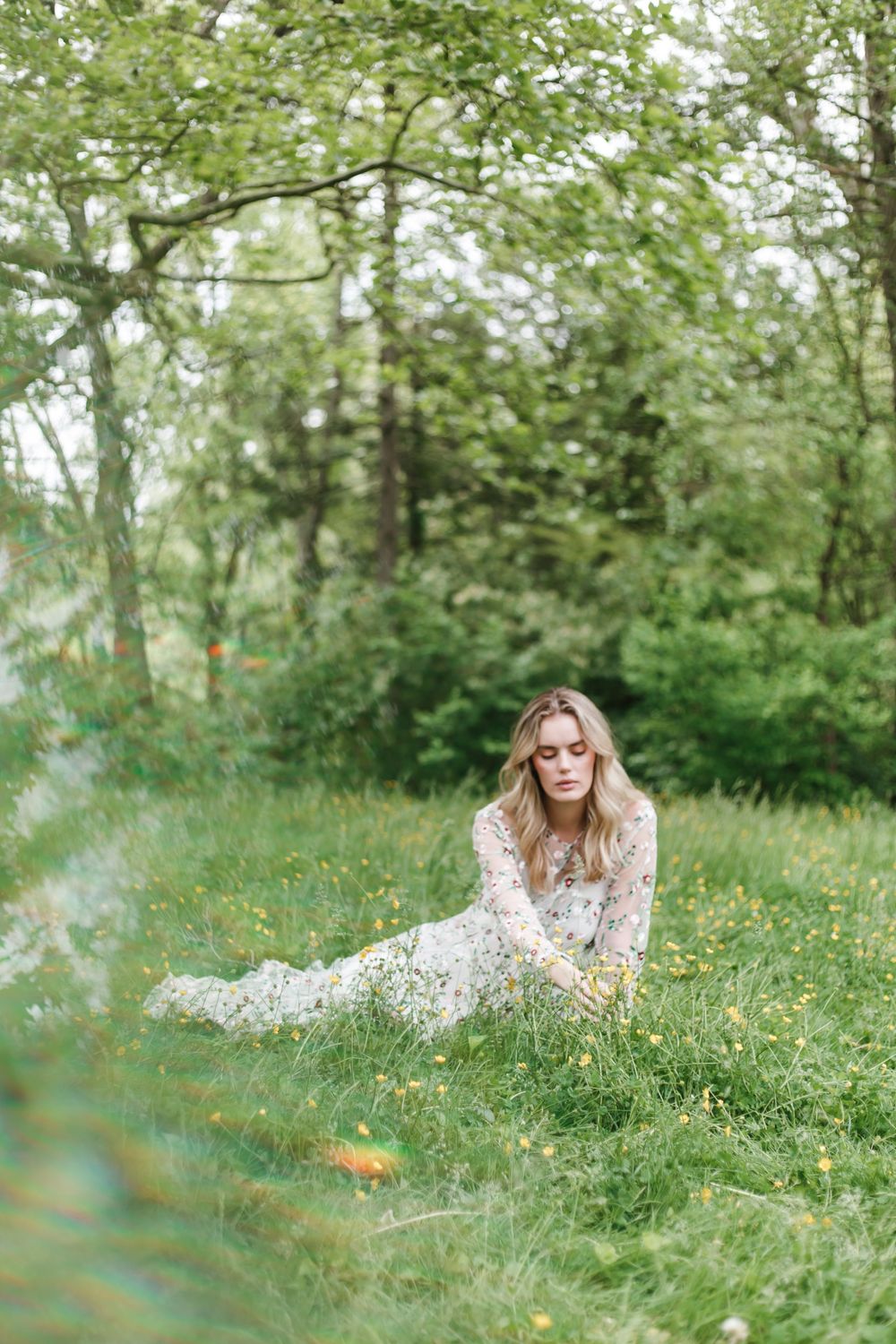 A person in a white dress lying in a dreamy meadow of wildflowers and grass on a sunny spring day.