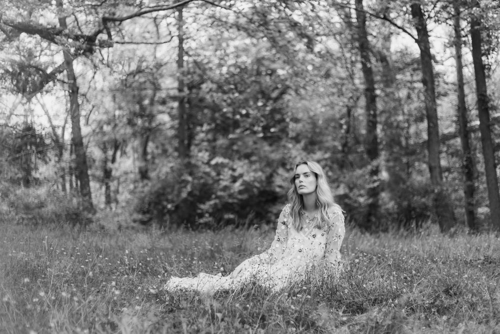 A black and white photo of someone reclining in a grassy meadow surrounded by trees.