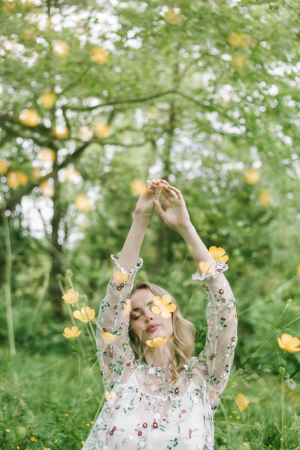 Ethereal spring scene with blooming yellow flowers and a floral dress among sunlit green foliage.