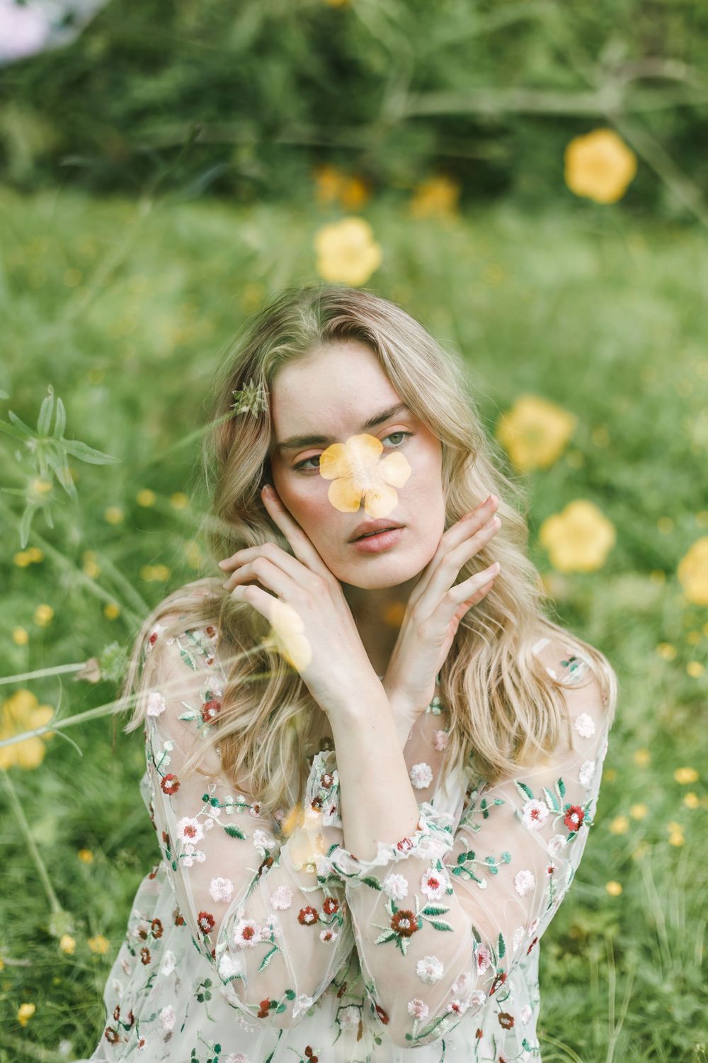 Ethereal spring portrait in flower field with soft yellow blooms and floral dress creating dreamy atmosphere.