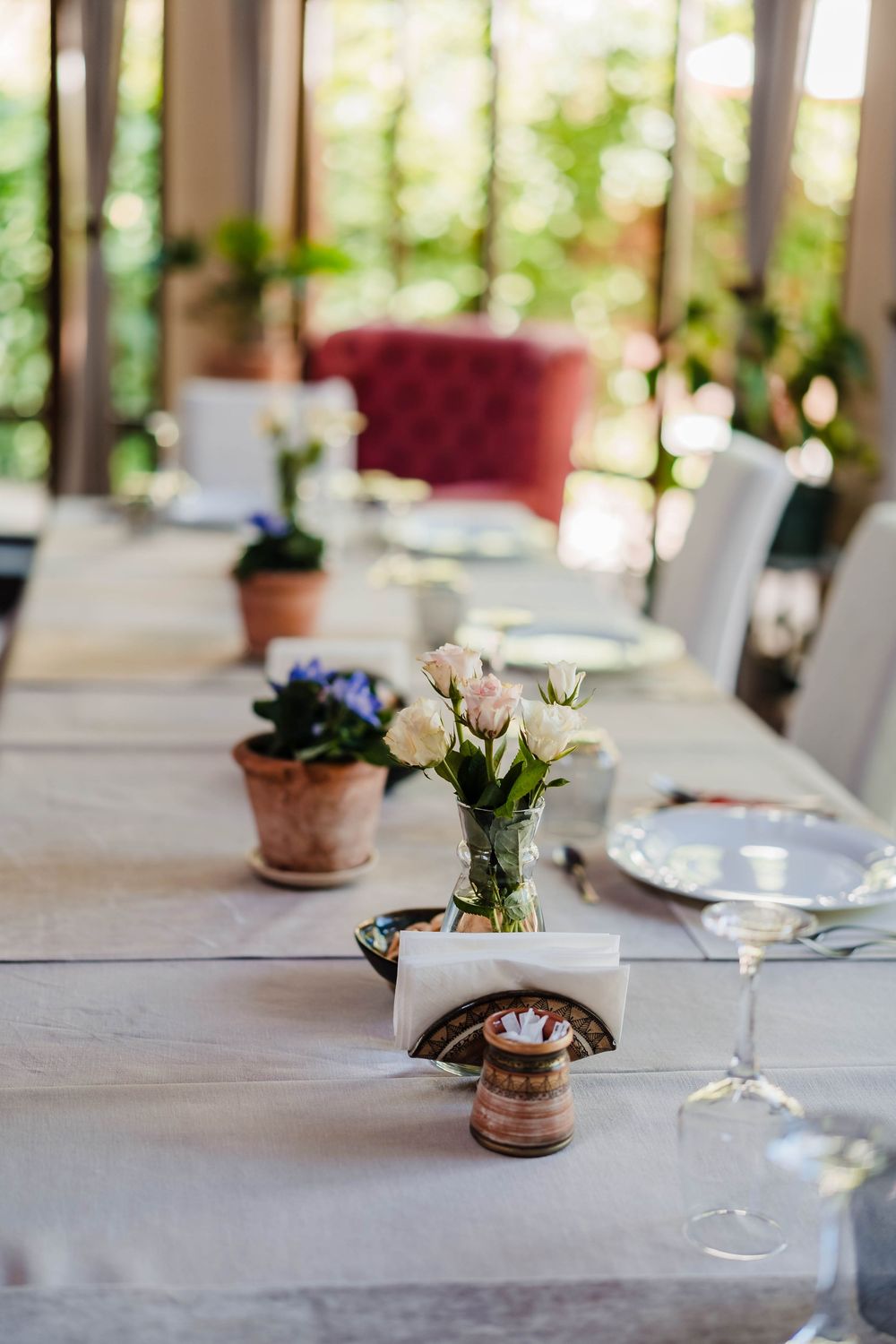 Elegant table settings with white linens and small potted flower centerpieces in a bright dining room.