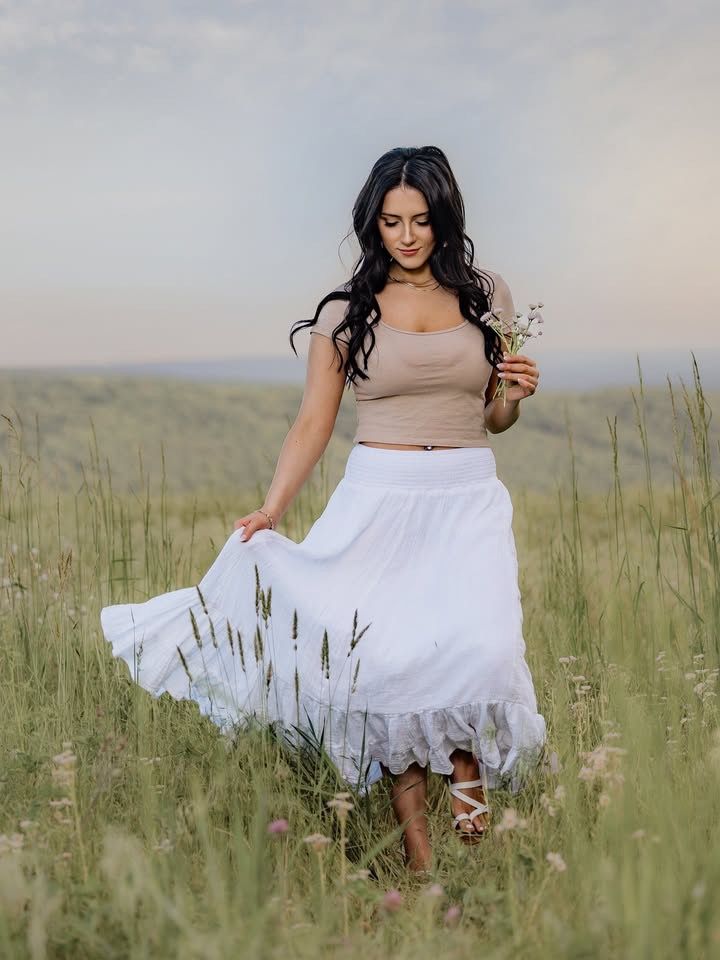 Person in flowing white dress walking through tall grass meadow.
