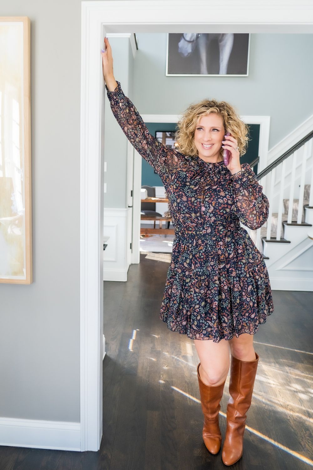 Stylish fall outfit with floral dress and brown boots in sunny home setting.