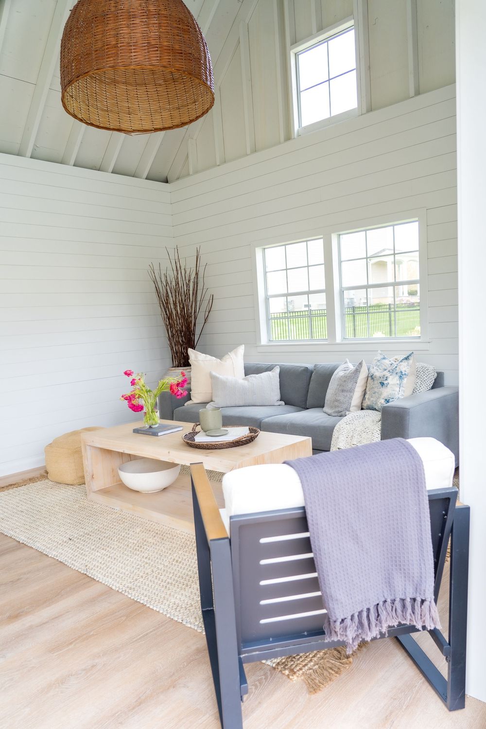 Cozy sunroom featuring gray sofa, woven pendant light, and white shiplap walls.