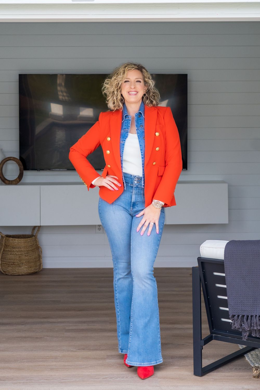 Modern fashion look featuring a bright red blazer with blue jeans and red heels on a porch setting.