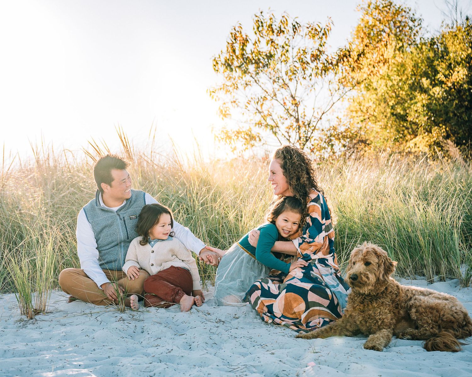 A family lounges on the beach with their dog during a warm golden sunset.