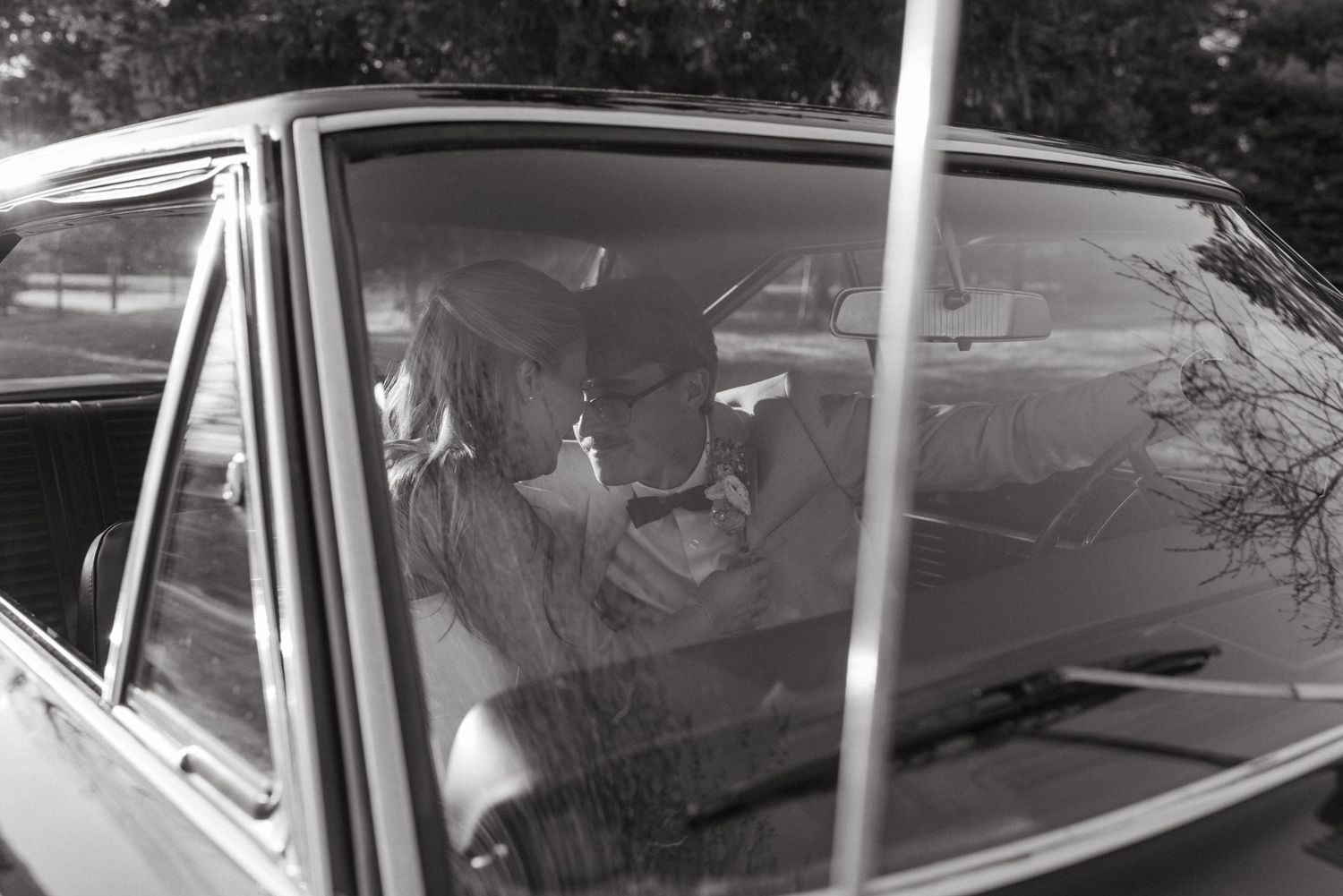 A vintage black and white photograph showing people seated inside a parked car in a candid moment.
