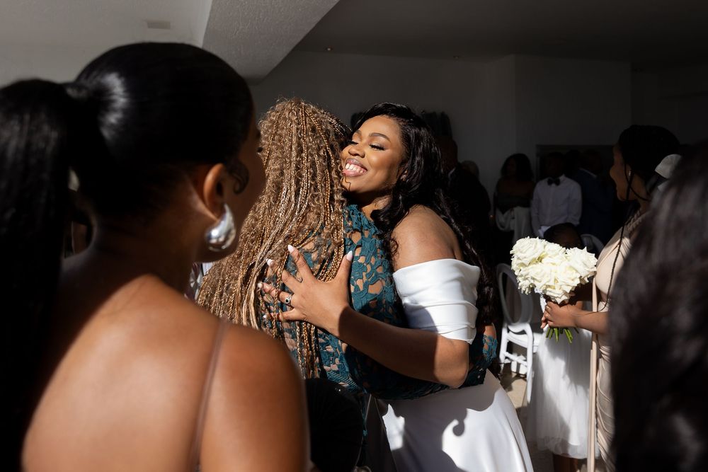 People share joyful embraces and congratulations at an elegant event with white floral decorations in the background.